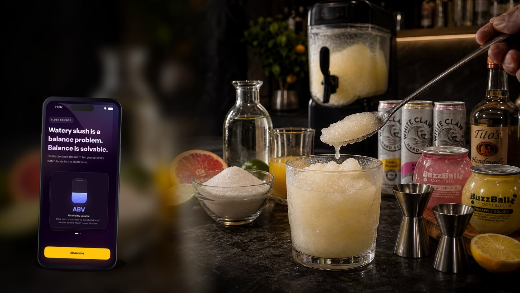 An iPhone showing Slushable ABV science placed on a dark bar counter beside pale hard-seltzer slush, White Claw cans, BuzzBallz cocktails, simple syrup, orange juice, sugar, citrus, and a Ninja SLUSHi.