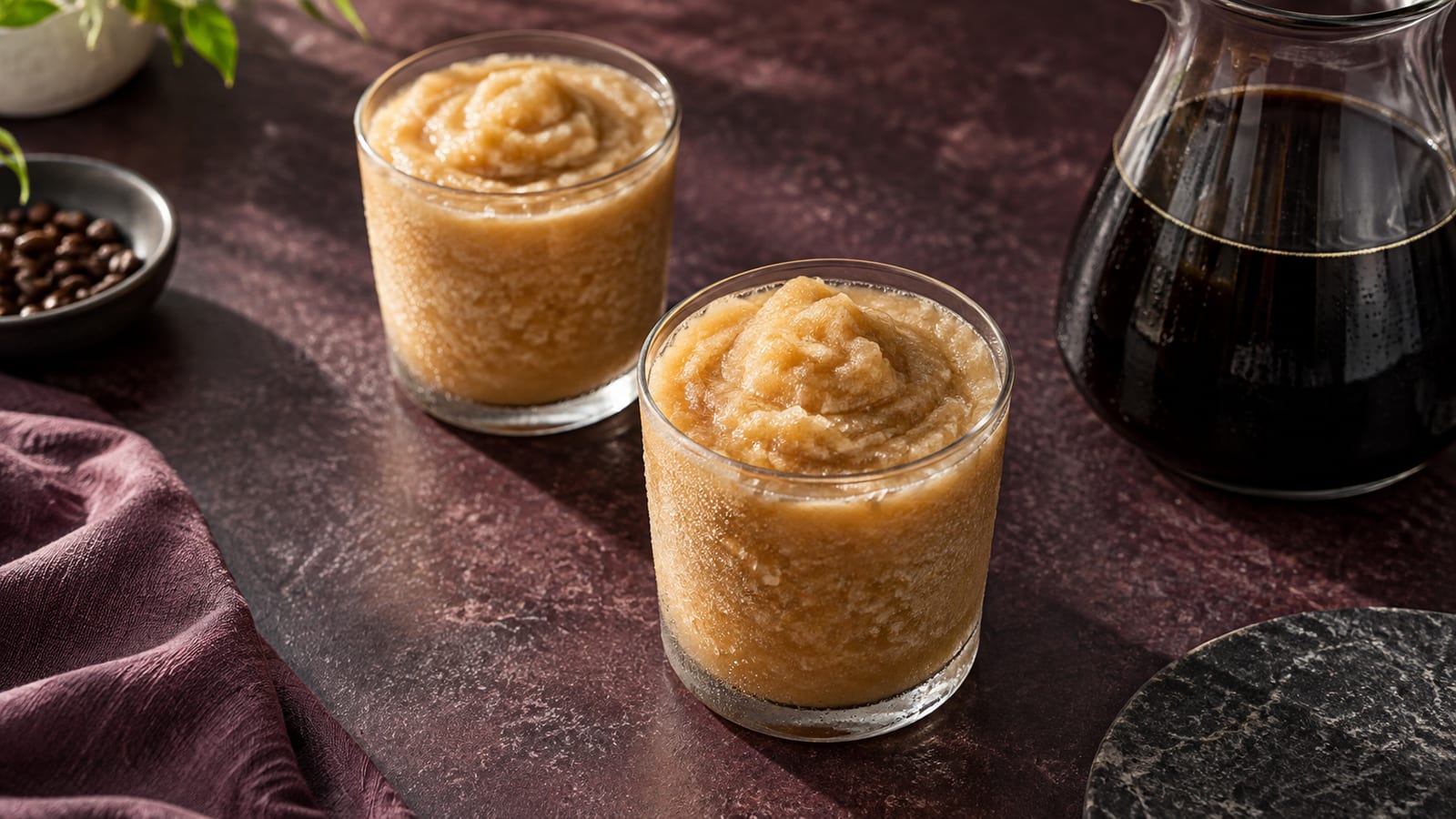 Illustrative caramel-coloured frozen coffee in two plain glasses beside a coffee carafe