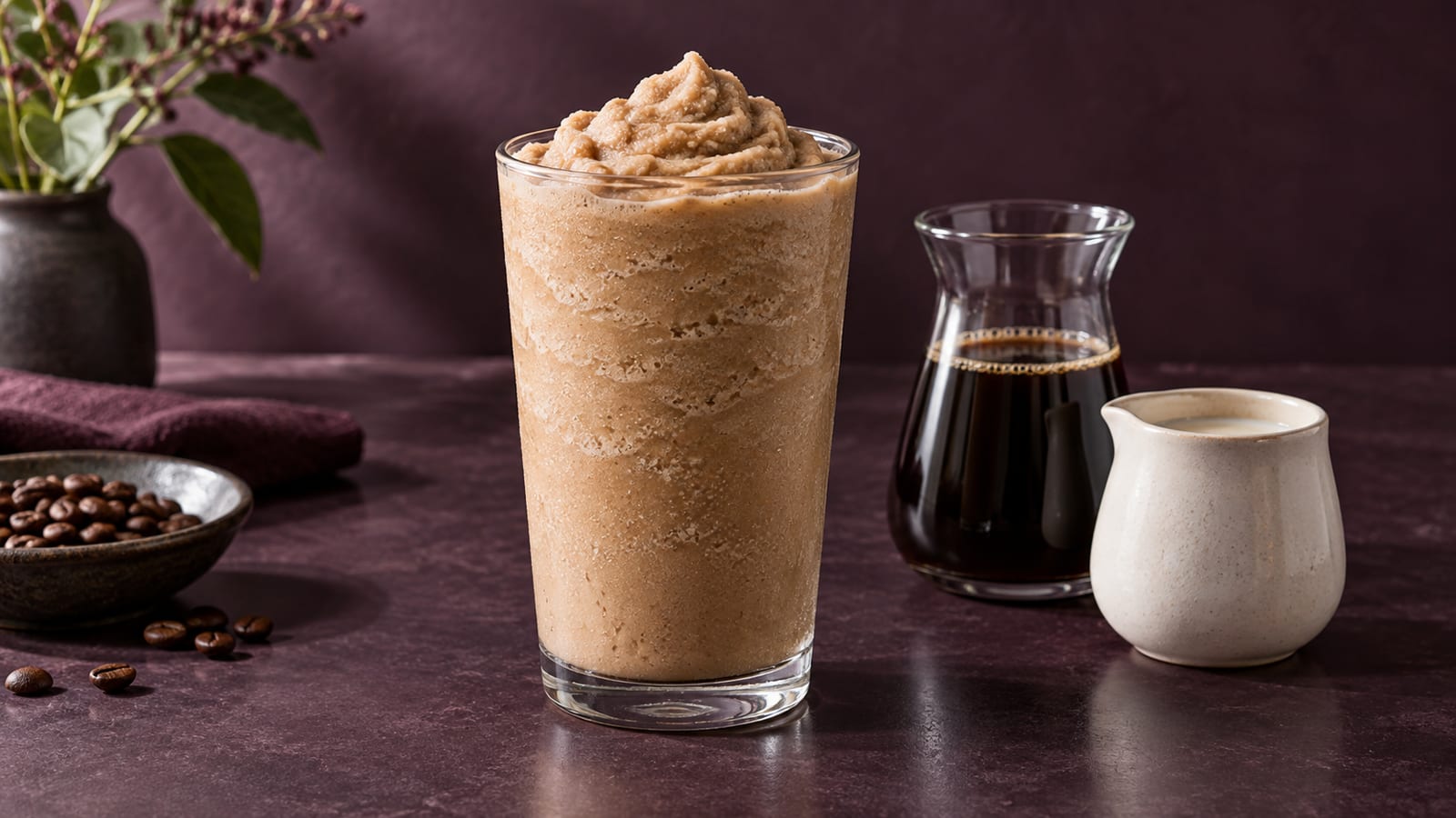 Illustrative coffee frappé beside black coffee and a small milk jug